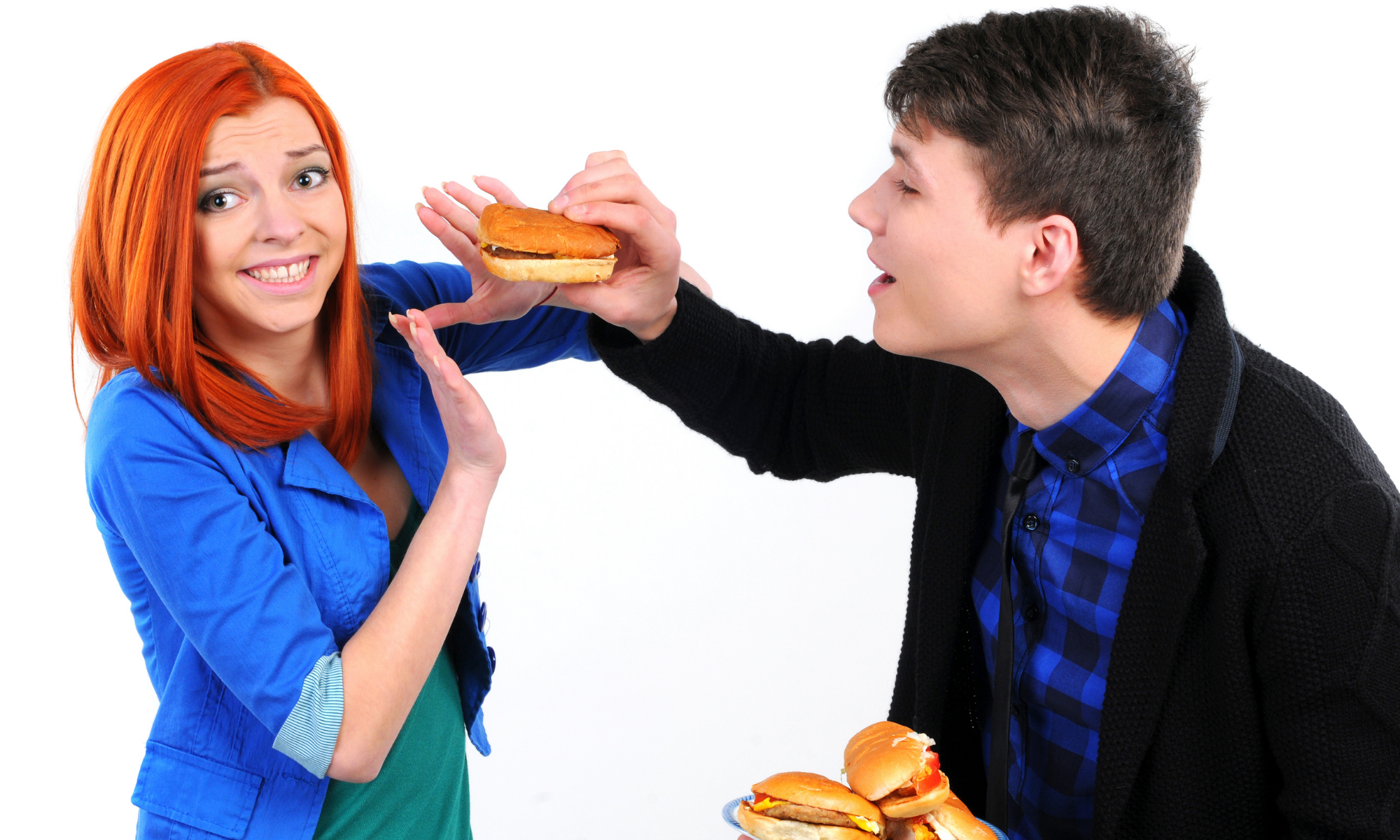Woman holds up hands in refusal of hamburger aggressively offered by man holding a plate of burgers Woman holds up hands in refusal of hamburger aggressively offered by man holding a plate of burgers
