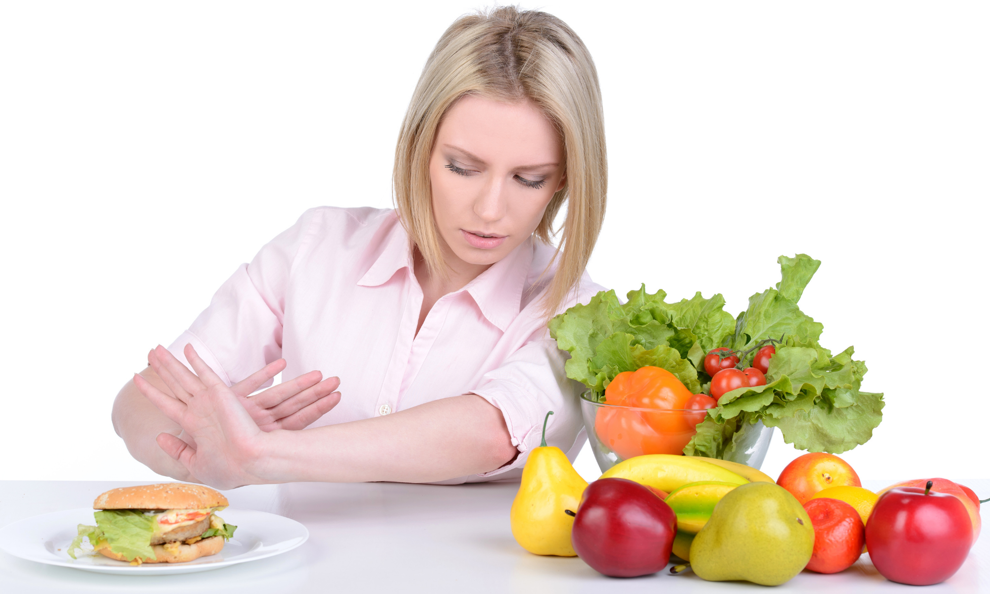 Woman holds out hands in refusal of hamburger on the left while various fruits and vegetables are on the right Woman holds out hands in refusal of hamburger on the left while various fruits and vegetables are on the right