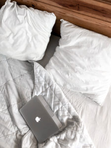 A half-closed laptop on a bed with ruffled sheets