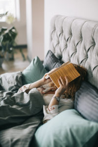Woman in bed with book over her face, indicating she fell asleep while reading