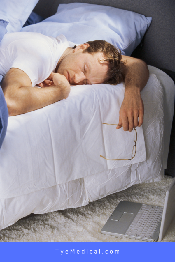 Man asleep on the bed with his arm hanging off the edge of the bed glasses in hand